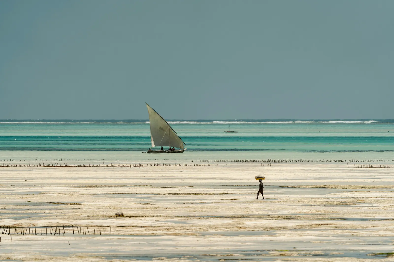 A visitor on Jambiani beach with a beached sailboat behind