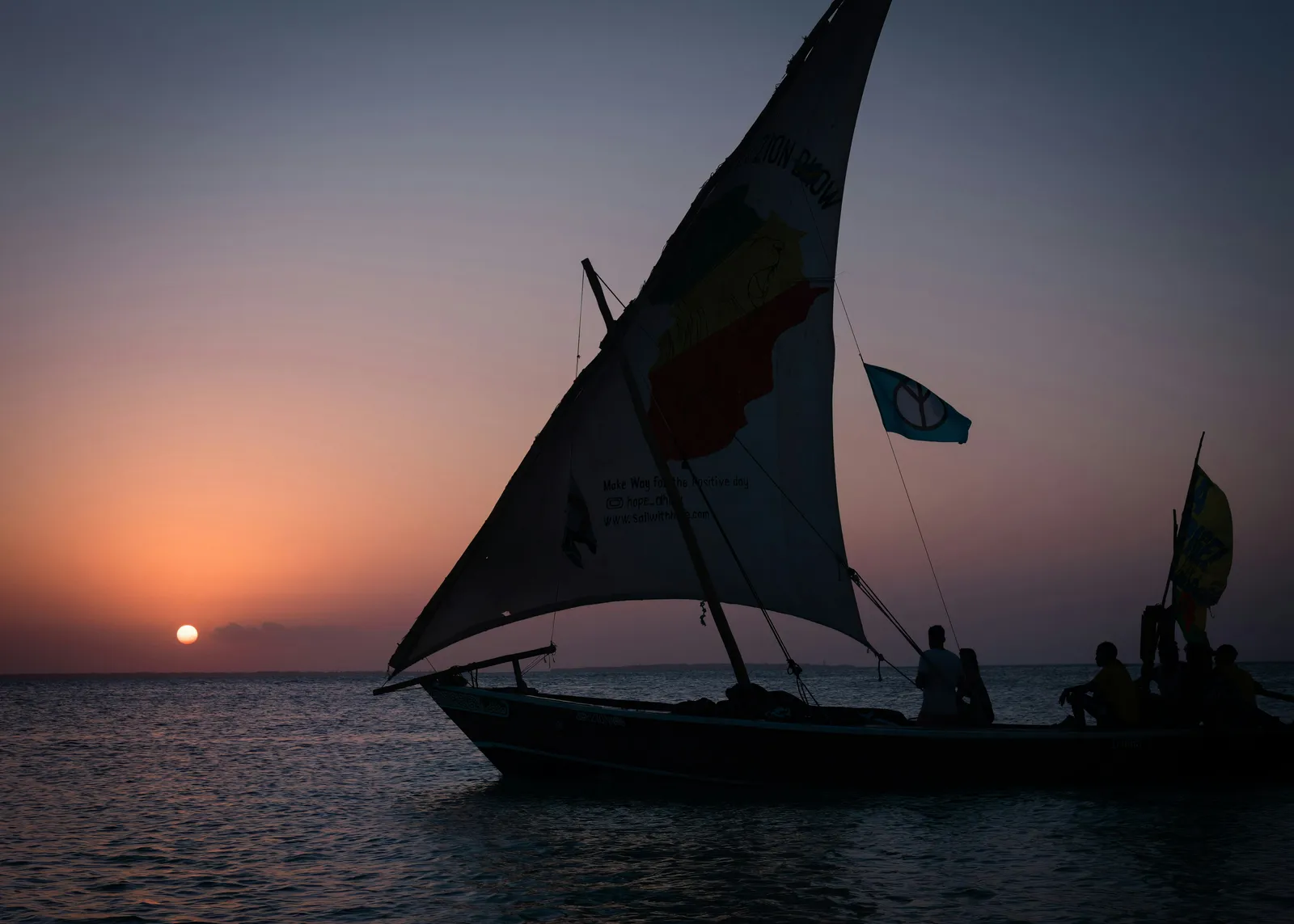 A sailboat with travellers on the water at sunset